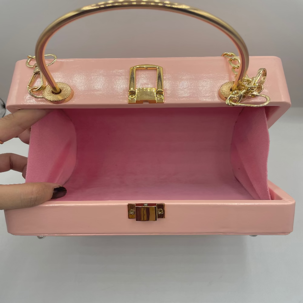 Pink handbag with gold accents held by a hand against a gray background