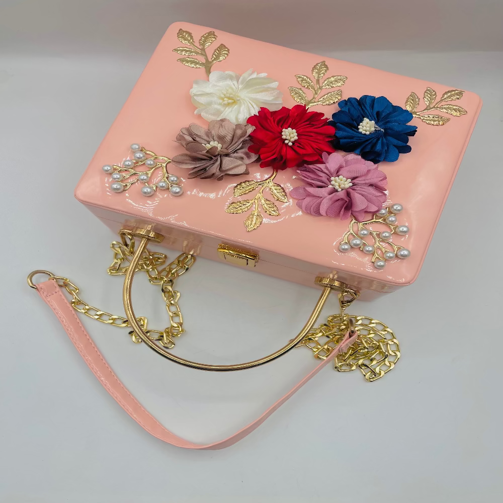 Pink handbag with floral decorations and gold chain handle on a light gray background