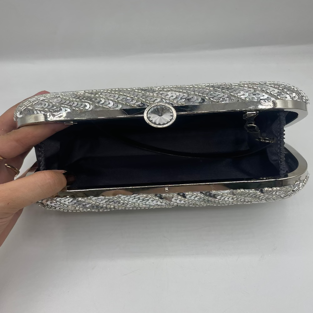 Silver clutch with intricate designs held by a hand on a white background